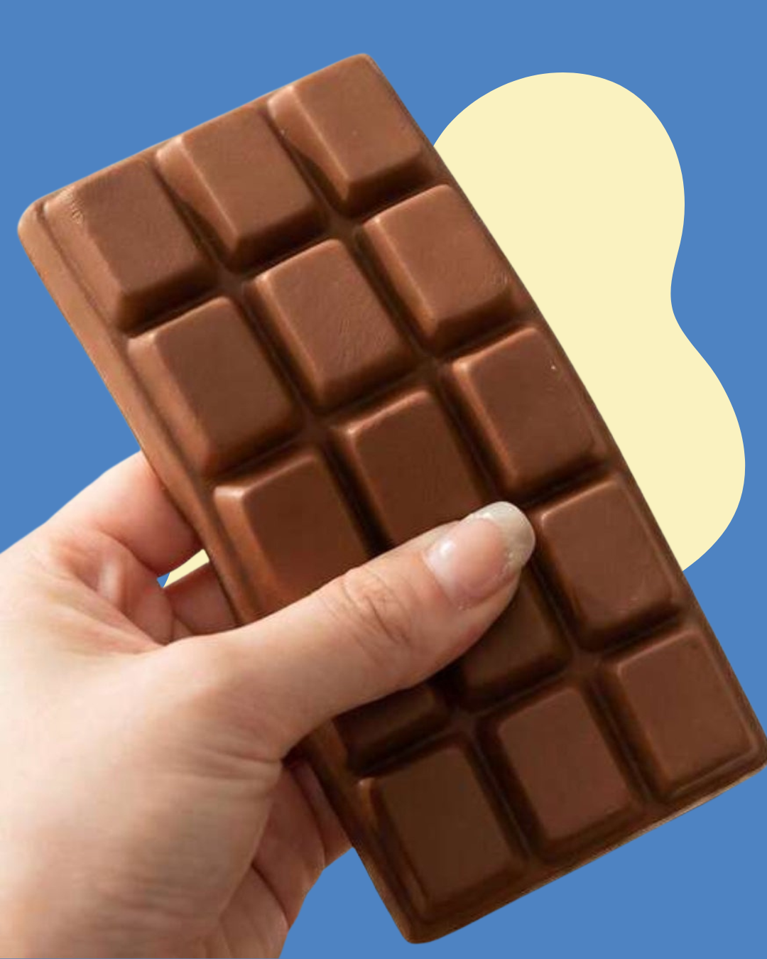 A hand holding a brown chocolate bar squishy toy against a blue background with a pale yellow abstract shape behind it.