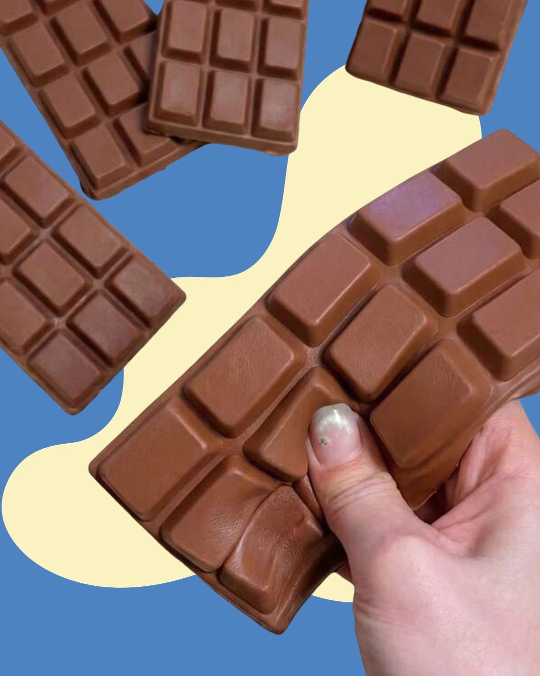 A hand with metallic silver nail polish holds a large, realistic brown chocolate bar squishy toy against a blue and cream abstract background, with several smaller chocolate bar squishy toys scattered around.